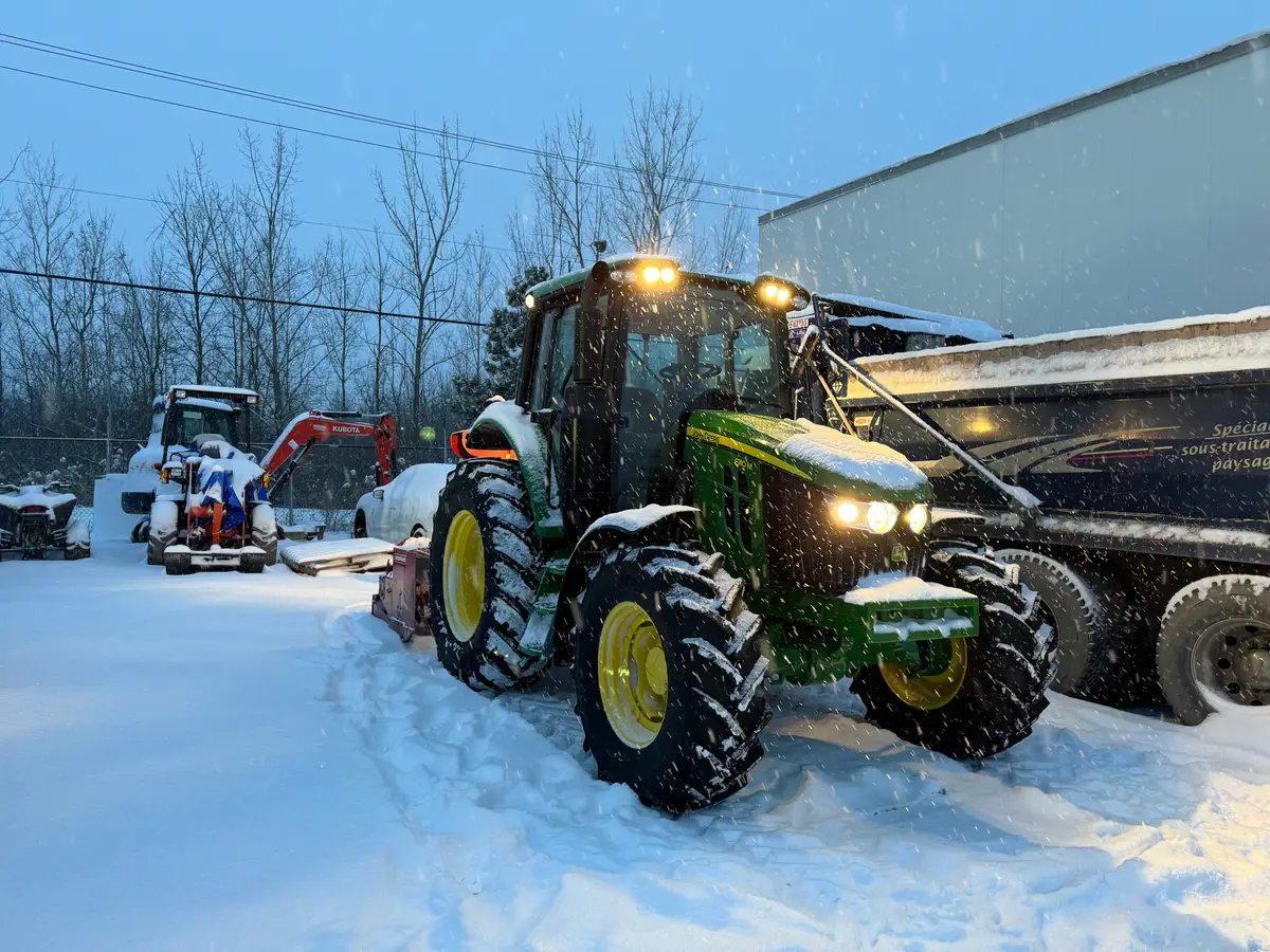 Tracteur de déneigement phares allumés sous la neige au crépuscule